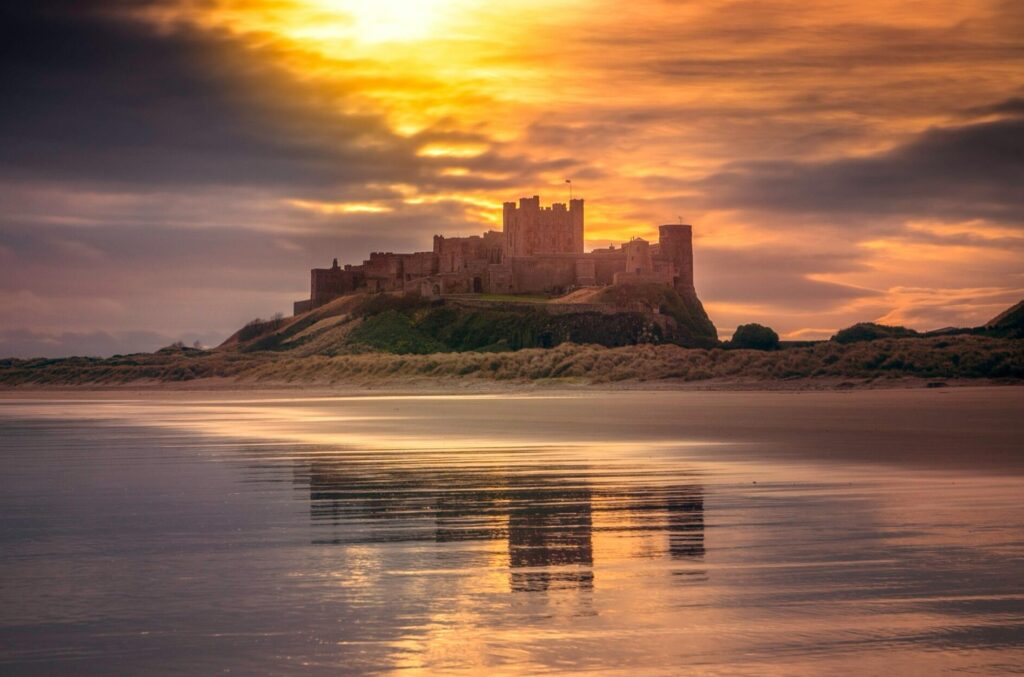 Stunning view of a castle reflecting on the tranquil beach at sunset, surrounded by a golden horizon.